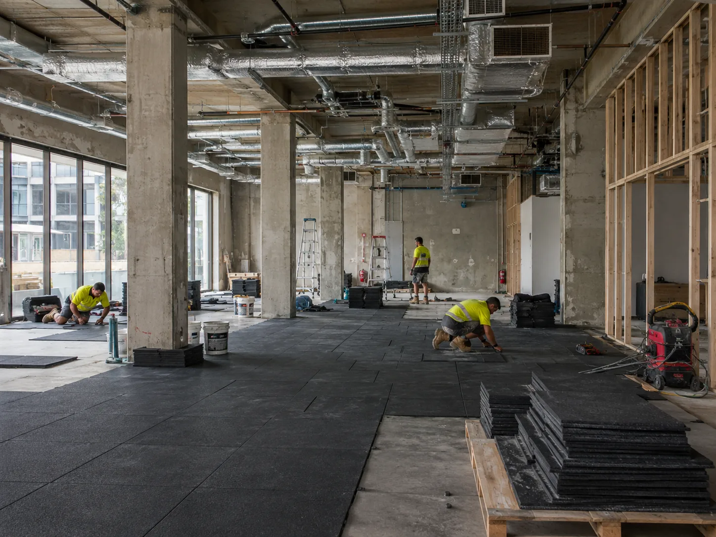 Commercial gym fitout construction site Sydney with trades installing rubber flooring and HVAC ductwork visible in ceiling