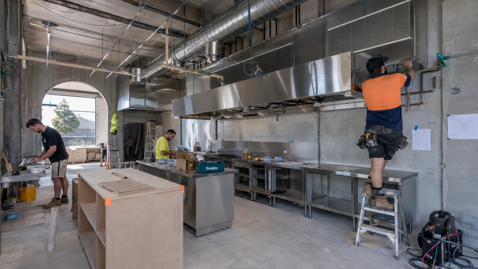 Commercial kitchen fitout Sydney under construction with stainless steel benches and ventilation ducts being installed